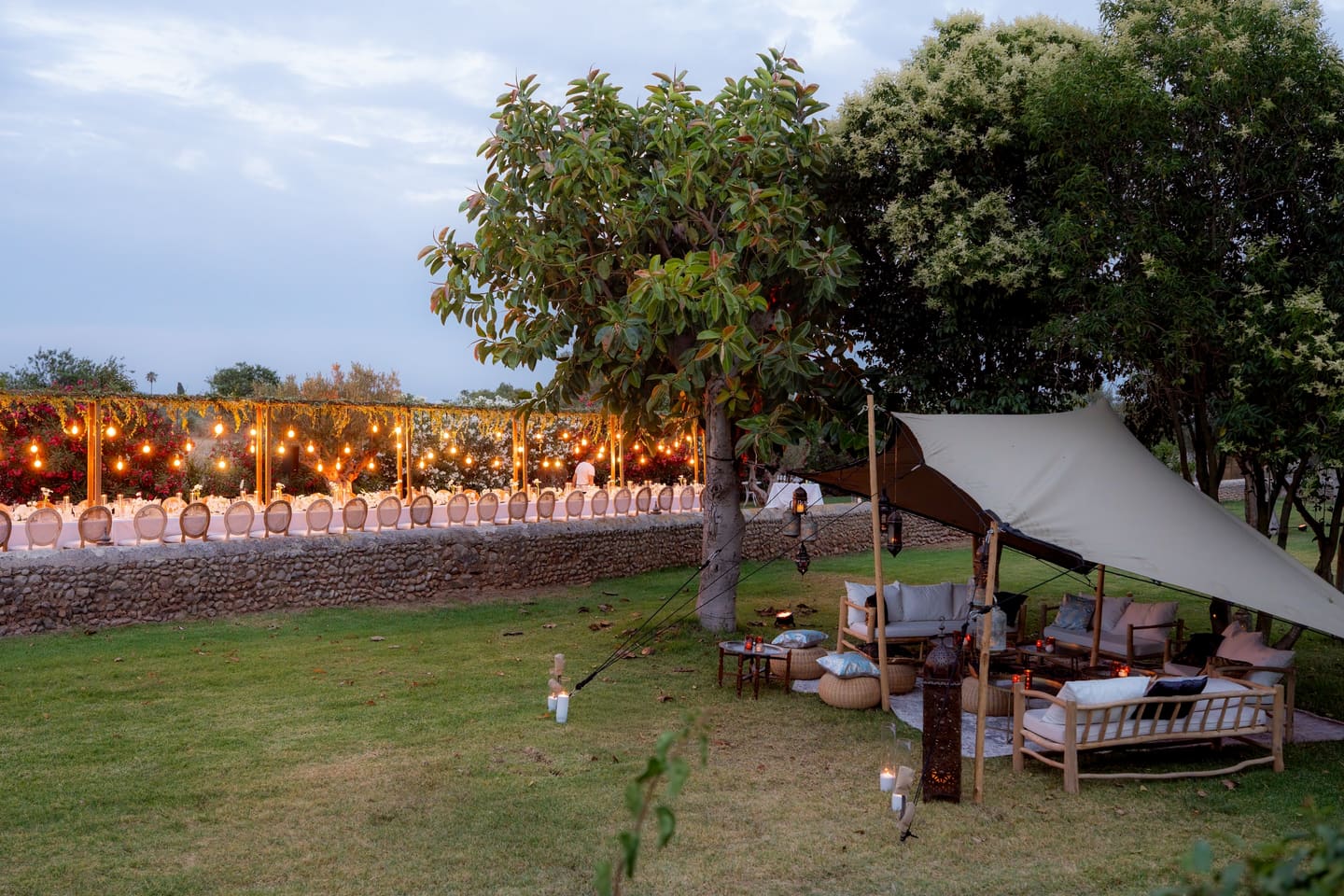 A private party on the lawn of a Mallorcan finca at dusk, tables lit with string lights and a lounge tent